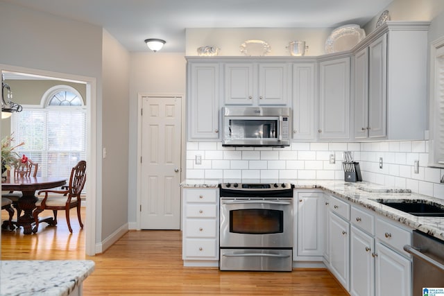 kitchen with backsplash, sink, light hardwood / wood-style flooring, and appliances with stainless steel finishes