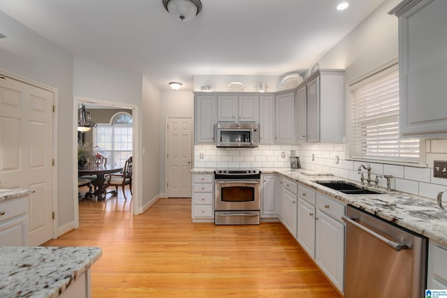 kitchen with light stone countertops, appliances with stainless steel finishes, tasteful backsplash, sink, and light hardwood / wood-style floors