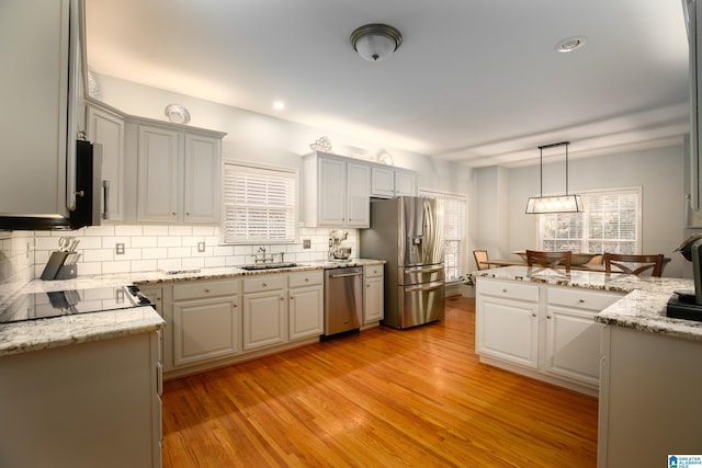 kitchen featuring decorative backsplash, pendant lighting, light hardwood / wood-style floors, and appliances with stainless steel finishes