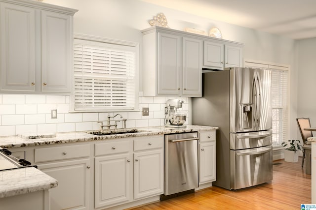 kitchen with sink, stainless steel appliances, tasteful backsplash, light stone counters, and light hardwood / wood-style flooring