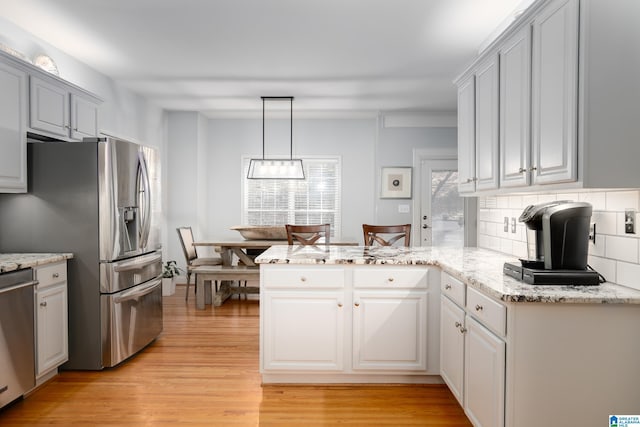 kitchen with decorative backsplash, decorative light fixtures, light hardwood / wood-style floors, kitchen peninsula, and stainless steel appliances