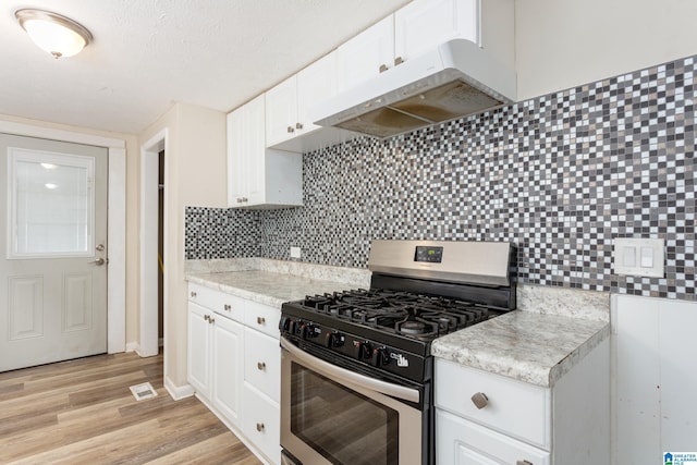 kitchen with light wood-type flooring, backsplash, stainless steel gas range oven, a textured ceiling, and white cabinets