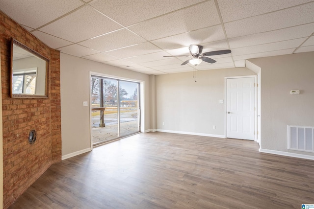 empty room with hardwood / wood-style floors, a paneled ceiling, and brick wall