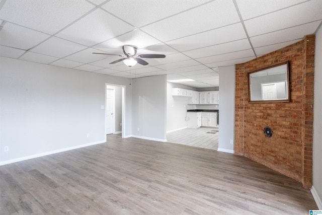 unfurnished living room with ceiling fan, a drop ceiling, and light wood-type flooring