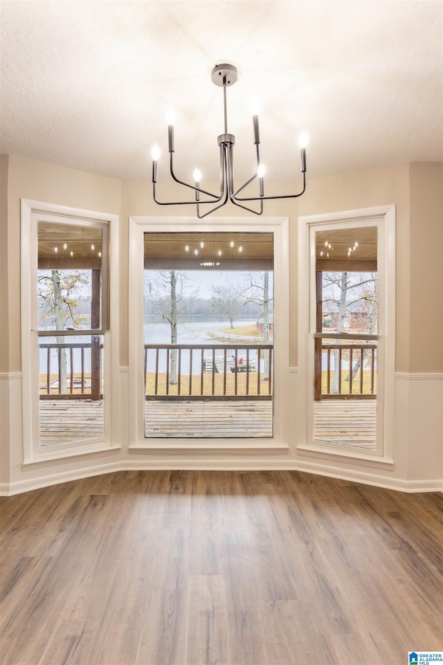 unfurnished dining area with a chandelier, plenty of natural light, and wood-type flooring