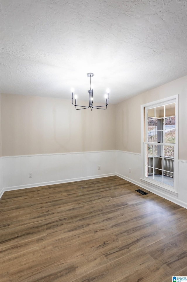 unfurnished dining area featuring dark hardwood / wood-style flooring, a textured ceiling, and an inviting chandelier