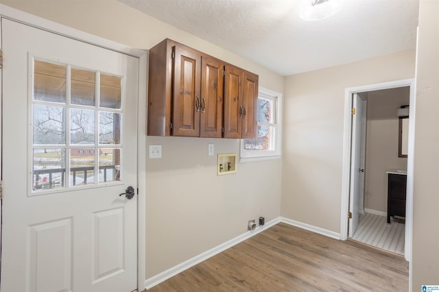 laundry room featuring electric dryer hookup, cabinets, hookup for a washing machine, light hardwood / wood-style flooring, and a textured ceiling