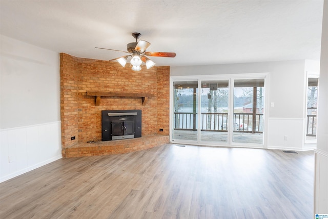 unfurnished living room featuring wood-type flooring, a wood stove, and ceiling fan