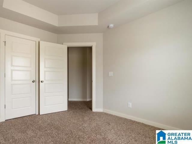 unfurnished bedroom with carpet flooring, a tray ceiling, and a closet