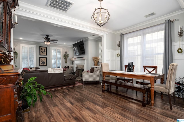 dining area with dark wood-type flooring, ceiling fan with notable chandelier, and ornamental molding