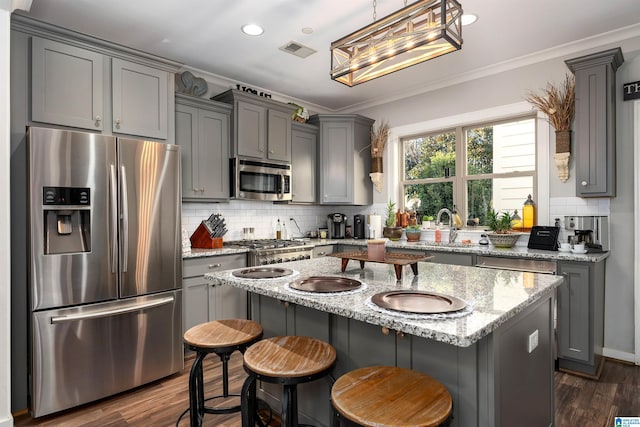 kitchen with a kitchen bar, dark hardwood / wood-style floors, appliances with stainless steel finishes, a kitchen island, and light stone counters