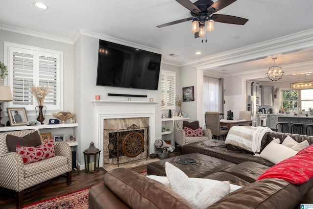 living room featuring dark hardwood / wood-style floors, ornamental molding, ceiling fan with notable chandelier, and a tile fireplace