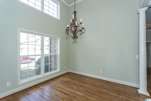 unfurnished room featuring crown molding, a towering ceiling, a notable chandelier, wood-type flooring, and decorative columns