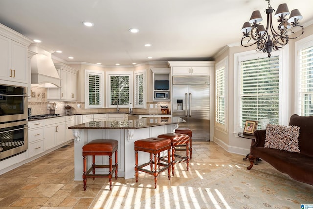 kitchen featuring built in appliances, dark stone countertops, a kitchen island, custom range hood, and decorative backsplash