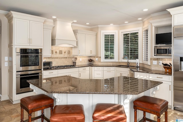 kitchen with appliances with stainless steel finishes, custom range hood, a breakfast bar, and dark stone counters