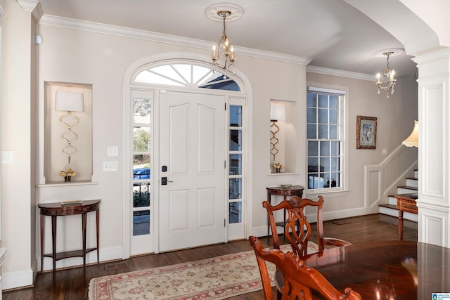 foyer entrance with crown molding, a chandelier, dark wood-type flooring, and decorative columns