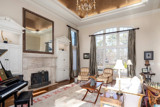 sitting room featuring hardwood / wood-style floors, ornamental molding, a notable chandelier, a raised ceiling, and a premium fireplace