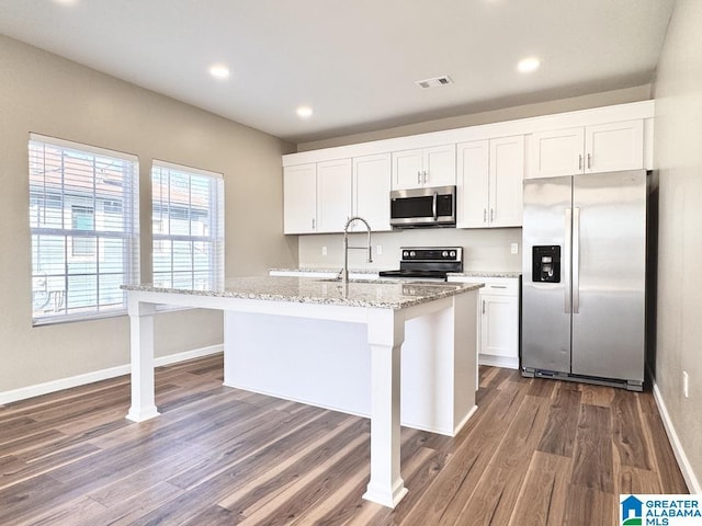 kitchen with light stone counters, dark hardwood / wood-style floors, an island with sink, white cabinets, and appliances with stainless steel finishes