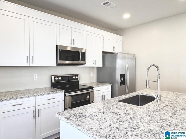 kitchen with light stone countertops, stainless steel appliances, white cabinetry, and sink