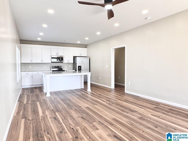 kitchen with white cabinetry, a center island with sink, hardwood / wood-style floors, and appliances with stainless steel finishes