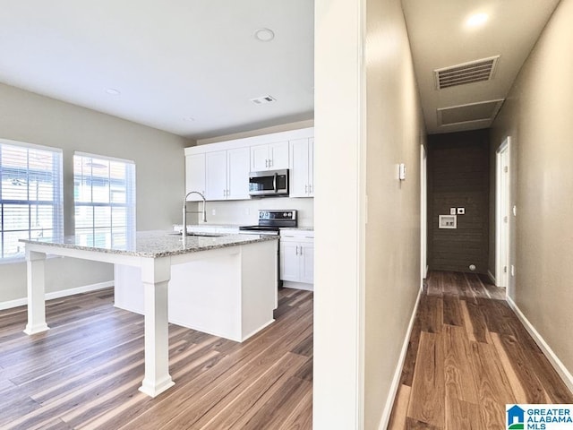 kitchen with appliances with stainless steel finishes, dark hardwood / wood-style flooring, sink, a center island with sink, and white cabinets