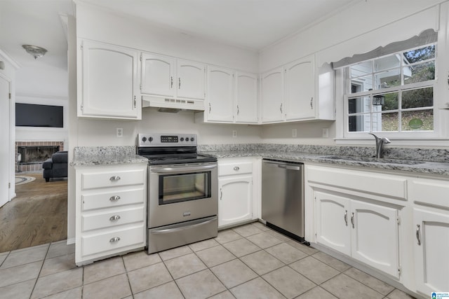 kitchen with appliances with stainless steel finishes, premium range hood, sink, a fireplace, and white cabinetry