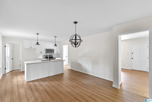 kitchen featuring light wood-type flooring, stainless steel appliances, decorative light fixtures, a center island with sink, and white cabinetry