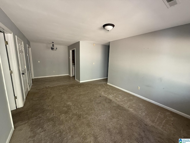 spare room with a chandelier and dark colored carpet