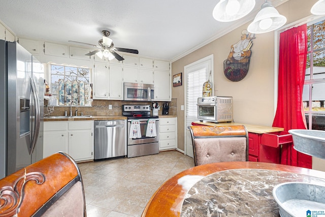 kitchen with backsplash, crown molding, sink, appliances with stainless steel finishes, and white cabinetry