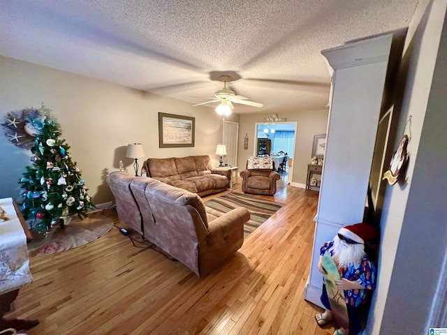 living room featuring ceiling fan, light wood-type flooring, and a textured ceiling