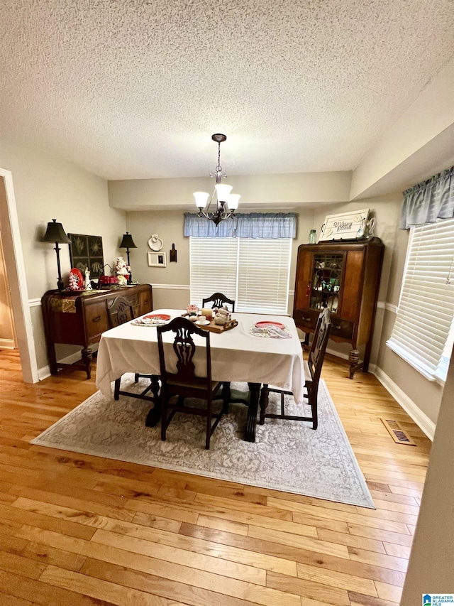 dining area featuring a textured ceiling, light wood-type flooring, and an inviting chandelier