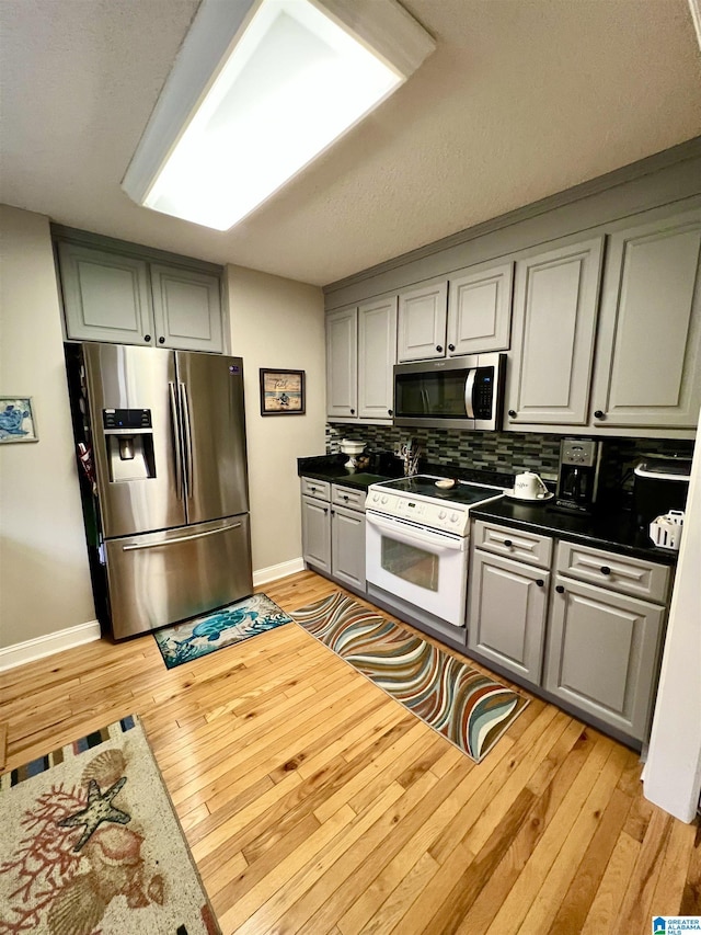 kitchen with gray cabinetry, light wood-type flooring, backsplash, and appliances with stainless steel finishes