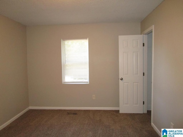 unfurnished room with a textured ceiling and dark colored carpet