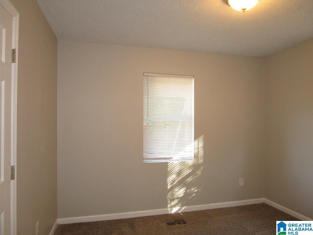 unfurnished room with a textured ceiling and dark colored carpet