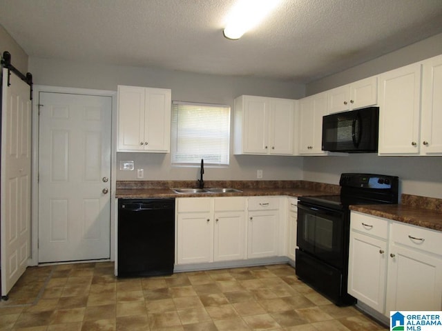 kitchen with black appliances, a barn door, white cabinets, and sink