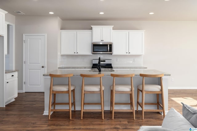 kitchen featuring white cabinetry, light stone counters, dark hardwood / wood-style flooring, decorative backsplash, and appliances with stainless steel finishes