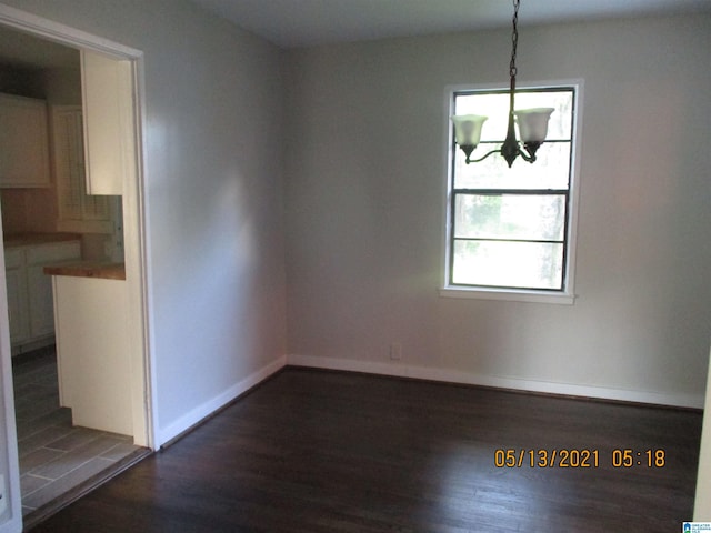 unfurnished dining area featuring an inviting chandelier and dark wood-type flooring