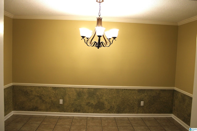 empty room with a chandelier, a textured ceiling, dark tile patterned flooring, and ornamental molding