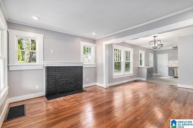 unfurnished living room with crown molding, plenty of natural light, wood-type flooring, and a brick fireplace