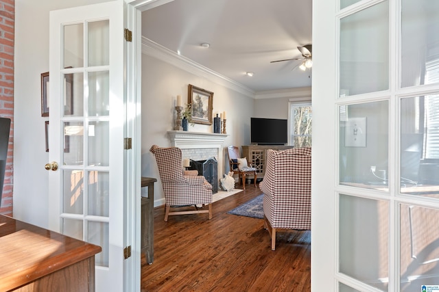 sitting room with ceiling fan, wood-type flooring, crown molding, and a brick fireplace