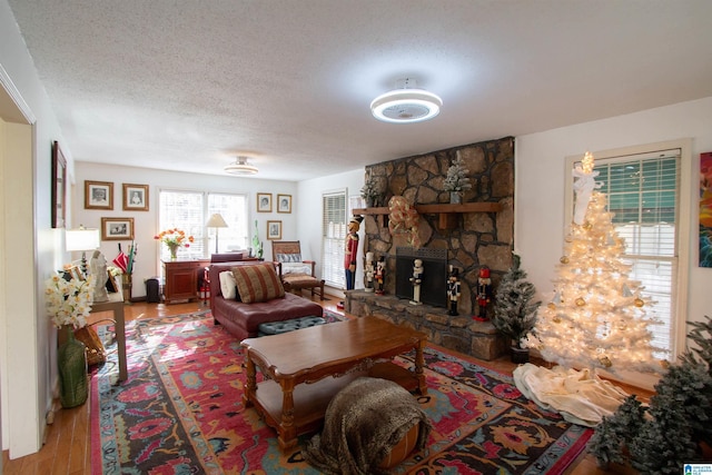 living room with a textured ceiling, light hardwood / wood-style floors, and a stone fireplace