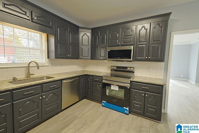 kitchen with tasteful backsplash, sink, light stone countertops, and appliances with stainless steel finishes