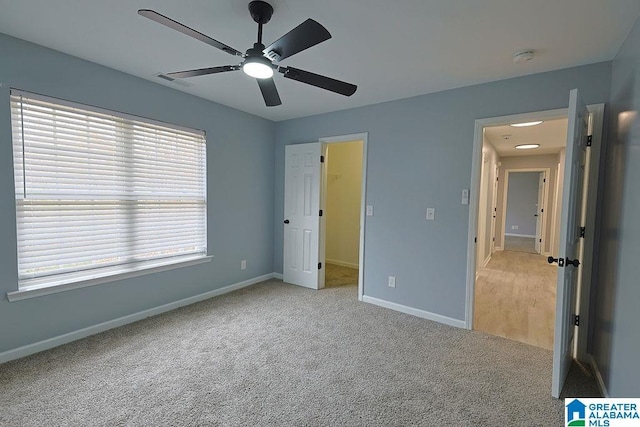 unfurnished bedroom with light carpet, a walk in closet, and ceiling fan