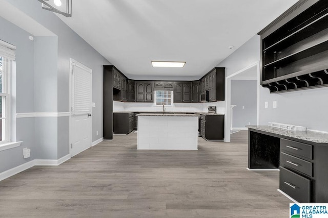 kitchen featuring appliances with stainless steel finishes, a center island, light stone counters, dark brown cabinets, and light wood-type flooring