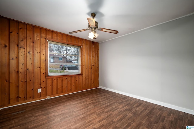 empty room featuring wood walls, wood finished floors, a ceiling fan, and baseboards