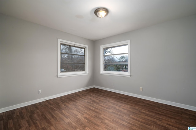 spare room featuring baseboards and dark wood-type flooring