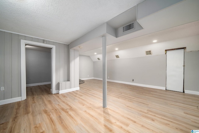 finished basement featuring baseboards, visible vents, a textured ceiling, and light wood finished floors