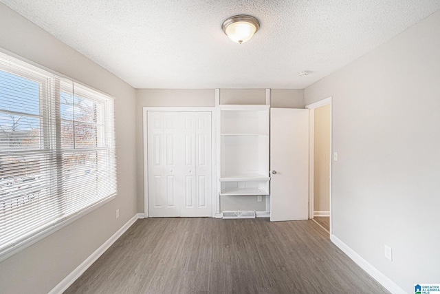 unfurnished bedroom with a textured ceiling, dark hardwood / wood-style flooring, and a closet