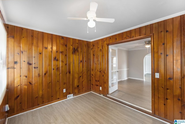 unfurnished bedroom featuring hardwood / wood-style floors, wooden walls, ceiling fan, and crown molding