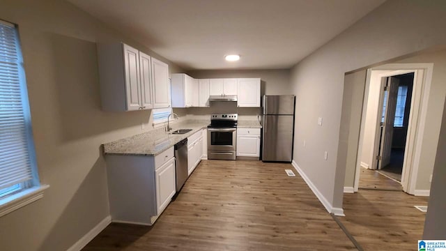 kitchen featuring appliances with stainless steel finishes, light stone counters, sink, white cabinets, and light hardwood / wood-style floors